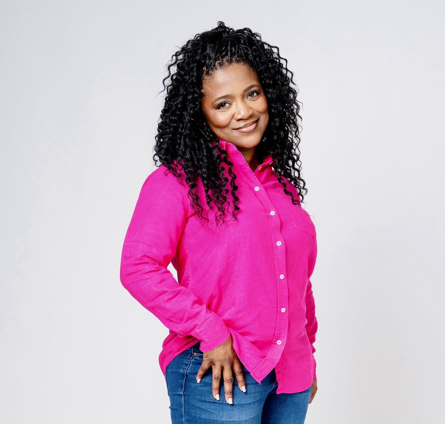 Ava Kay Rose smiling in a vivid pink blouse and jeans against a light studio background