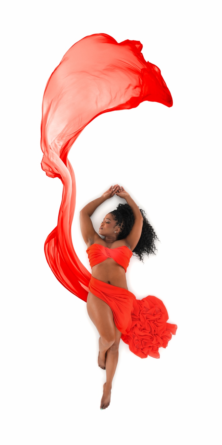Ava Kay Rose posed in a sculptural red ensemble beneath a sweeping arc of flowing red fabric